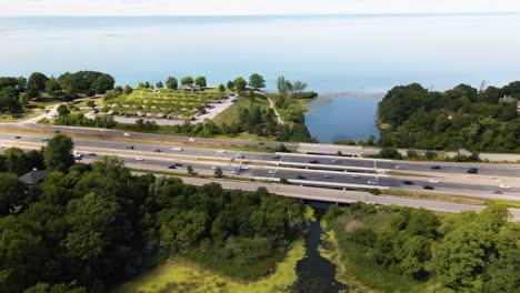 aerial view of cars driving on a highway through a green park next to the lake ontario in canada