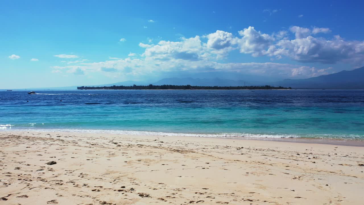 bali, indonesia, playa de arena paradisíaca, paisaje marino con una pequeña isla tropical y barcos navegando en la distancia, cielo azul brillante con nubes blancas esponjosas
