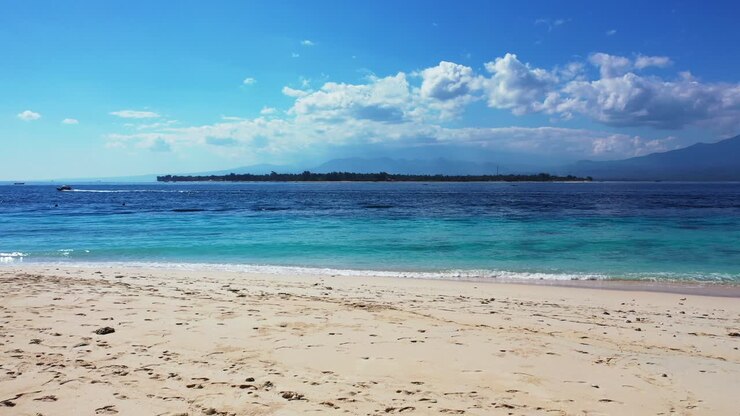 Bali, Indonesia, paradise sandy beach, seascape with small tropical island and boats sailing in the distance, bright blue sky with fluffy white clouds