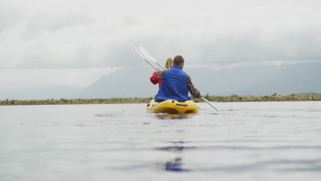 Pareja-Caucásica-Pasando-Un-Buen-Rato-En-Un-Viaje-A-Las-Montañas,-Haciendo-Kayak-Juntos-En-Un-Lago