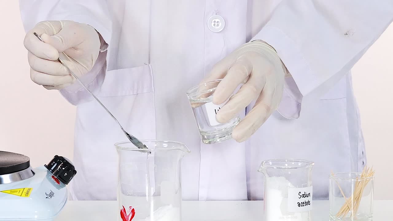 A scientist mixes a white powder into a clear liquid using a spoon in a laboratory setting.