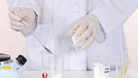 a scientist mixes a white powder into a clear liquid using a spoon in a laboratory setting.