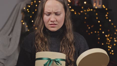 curious woman opening present for christmas, looking unhappy and upset