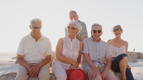 Porträt-älterer-Freunde,-Die-Im-Sommergruppenurlaub-Auf-Felsen-Am-Meer-Sitzen