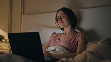 closeup girl working computer in bed. smiling busy freelancer typing computer