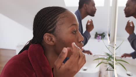 African-american-couple-using-face-cream-and-looking-in-bathroom-mirror-in-the-morning,-slow-motion