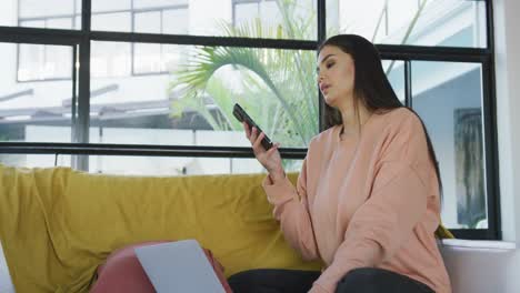 Video-Einer-Glücklichen-Gemischtrassigen-Frau,-Die-Auf-Dem-Sofa-Sitzt-Und-Ihr-Smartphone-Benutzt