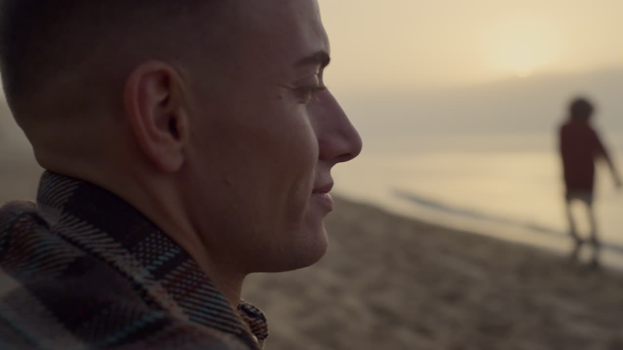 hombre sonriente mirando el paisaje del mar al amanecer. tipo positivo sentado en la playa