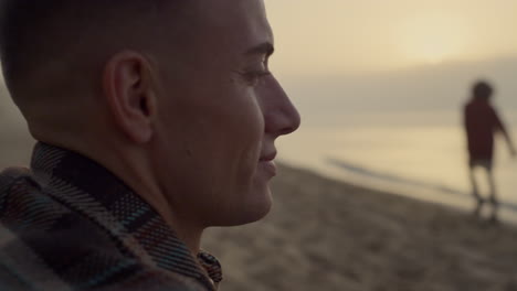 hombre sonriente mirando el paisaje del mar al amanecer. tipo positivo sentado en la playa