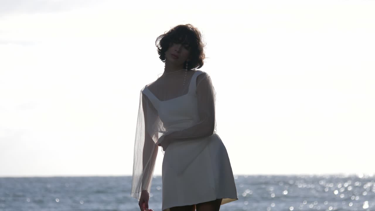 Donna in mini abito bianco in posa su uno sfondo di paesaggio marino naturale. Slow motion