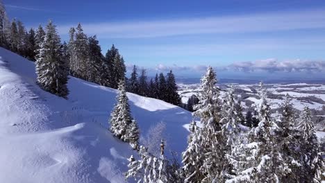 Two-people-ascend-Hundwiler-Hoehe-through-deep-snow,-aerial-reveal