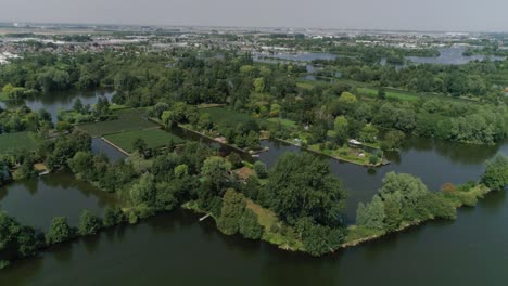 aerial slomo wide shot of dutch countryside surrounded with small rivers, green trees and bushes, tilting up, revealing small town in background