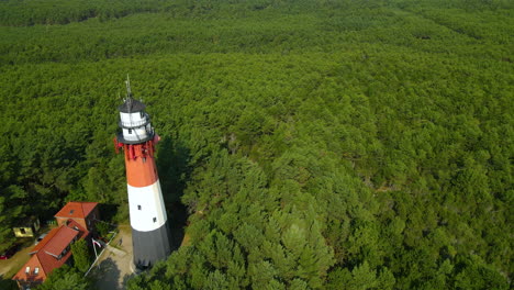 the drone slow pulls out and reveals stilo lighthouse and green forest around it - lighthouse located in osetnik on the polish coast of the baltic sea, close to the village of sasino, aerial close-up