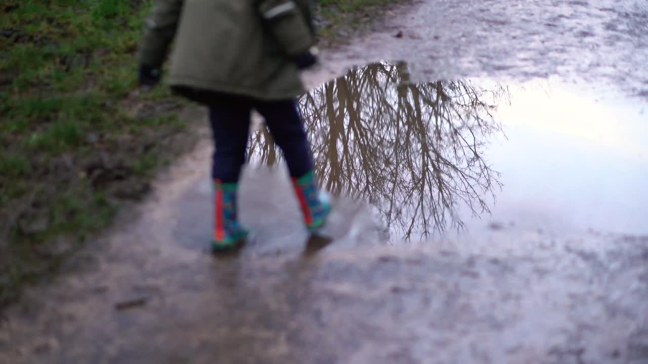 un niño caminando por un charco fangoso con botas de agua coloridas