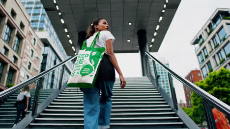 woman walks up city stairs carrying a green tote bag