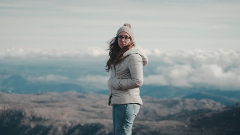 Una-Joven-Pensativa-Con-Chaqueta-Gris,-Sombrero-Y-Bufanda-Contempla-Un-Impresionante-Paisaje-Montañoso-En-Una-Caminata