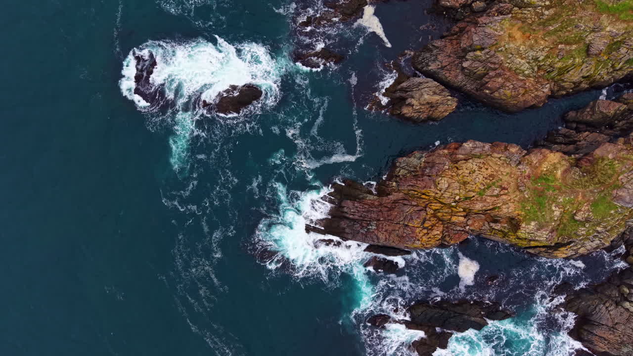 Waves crash against rugged coastal rocks under a bright sun, capturing the essence of nature's beauty at the ocean's edge in a stunning landscape