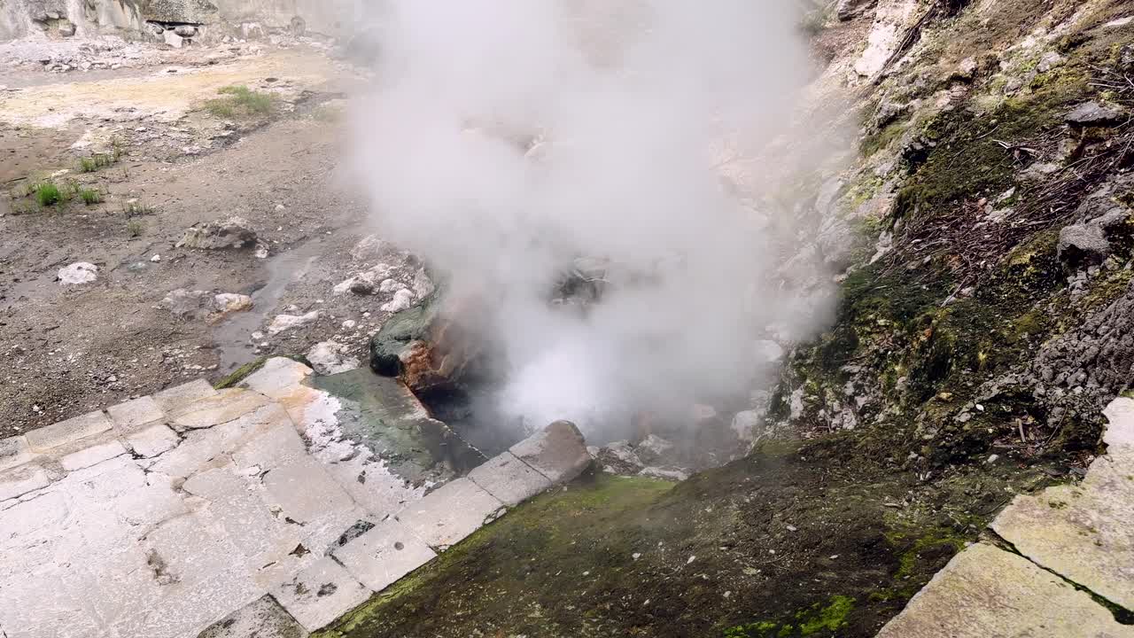 Vapor subindo de uma fumarola geotérmica em área vulcânica rochosa nos Açores.