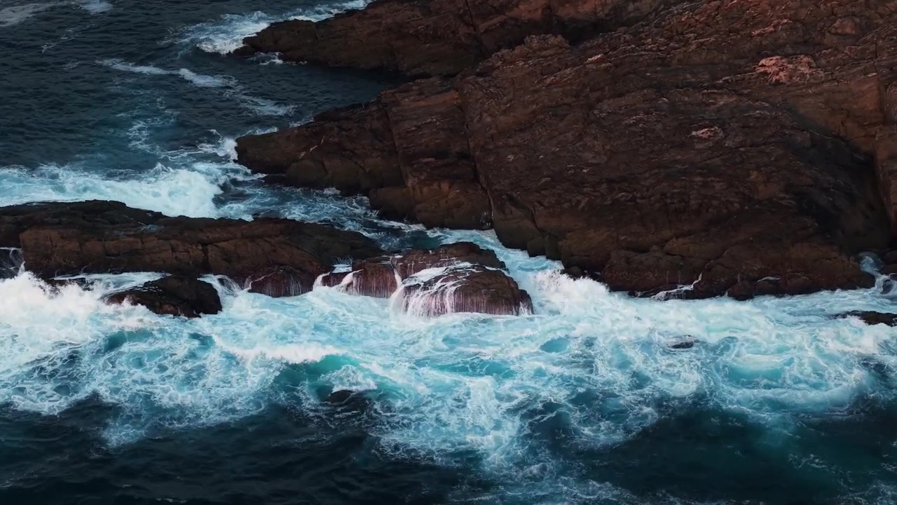 Drone che vola verso le onde atlantiche che si infrangono contro scure rocce costiere lungo la frastagliata costa della Galizia in Spagna.