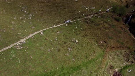 Vista-Aérea-De-Dos-Autos-Conduciendo-Por-Una-Difícil-Y-Empinada-Carretera-De-Montaña-Con-Un-Auto-Todoterreno-En-El-Paisaje-Montañoso-De-Suiza