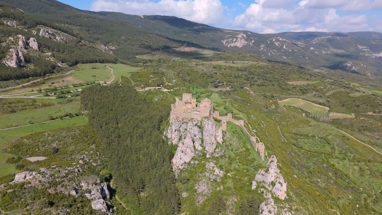 Cinematic drone shot flying forward alongside a medieval castle perched on a cliff, surrounded by pine forest, rugged hills, and cultivated countryside under a partly cloudy sky