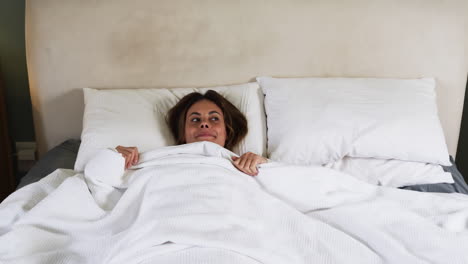 woman relaxing in bed, smiling under cozy white blanket at home