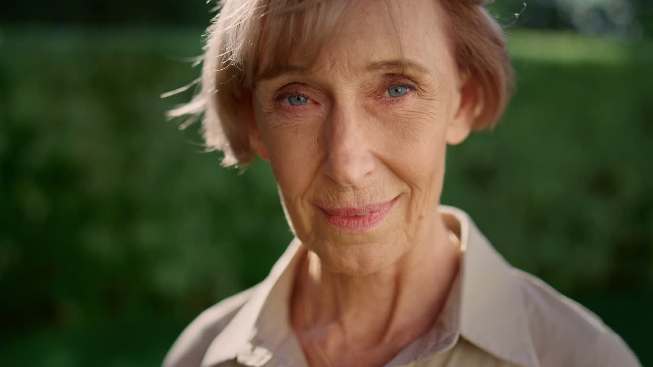 Smiling senior woman posing at camera in summer garden. Senior lady looking down