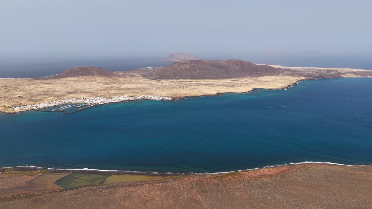 Picturesque View Of La Graciosa Island In Spain, With Volcanic Terrain, Coastal Village, And Blue Atlantic Waters. wide aerial shot