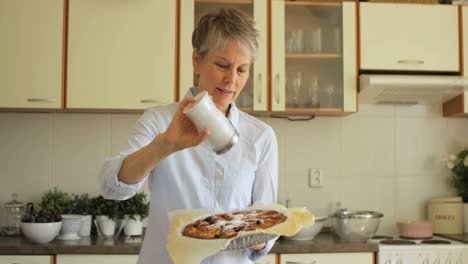 Senior-woman-sprinkling-freshly-baked-tart-with-powdered-sugar