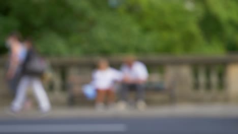 Defocused-Shot-of-Traffic-and-People-Moving-In-Front-of-Couple-Sat-On-Bench-01