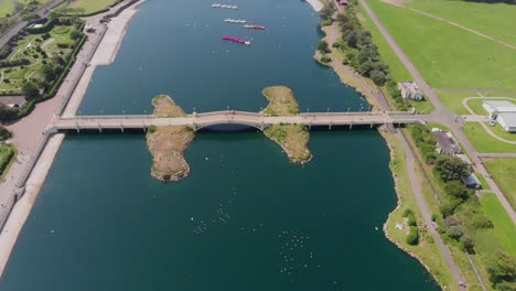 drones volando sobre el puente en el lago en la ciudad costera, gente caminando por el puente en un día soleado