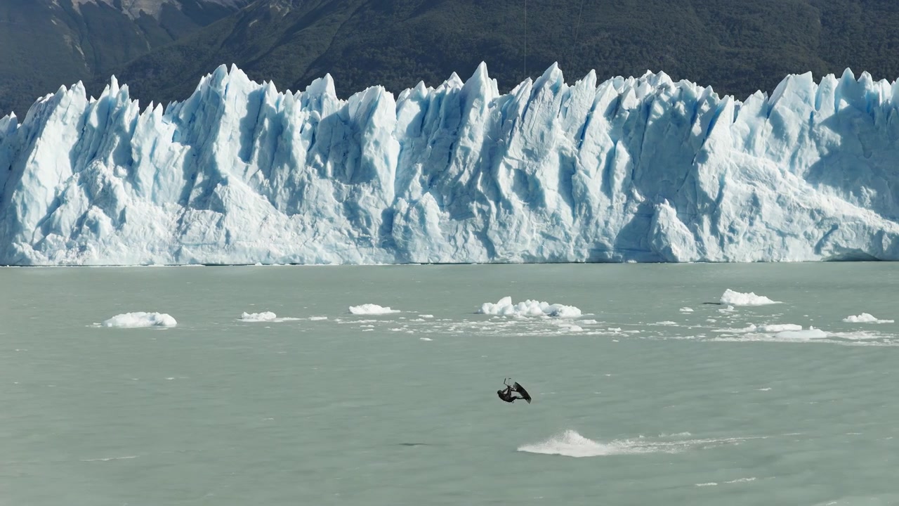 Un drone riprende un kitesurfer in rapido movimento attraverso il Lago Argentino sotto il Ghiacciaio Perito Moreno vicino a El Calafate, Santa Cruz, Argentina, circondato da ghiaccio galleggiante in acque glaciali, ripresa con drone