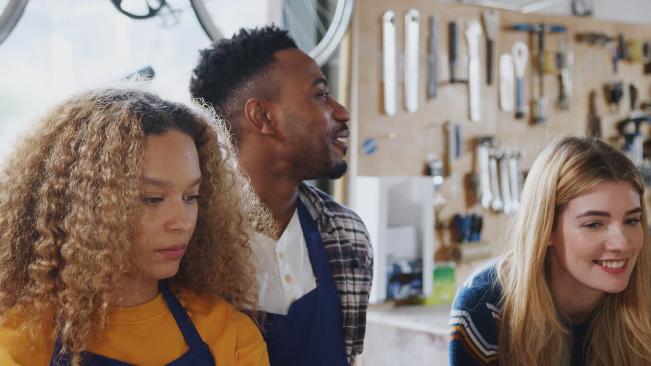 Multi-Cultural Team Of Trainees In Workshop Learn How To Assemble Hand Built Bicycle Frame Together