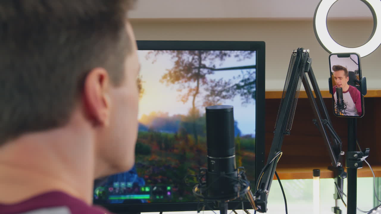 hombre jugando en casa sentado en el escritorio transmisión en vivo juego de disparos desde el teléfono móvil