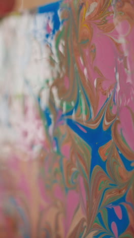 little girl looks at picture with abstract ebru patterns held by woman in art studio extreme closeup slow motion. colorful marbling technique