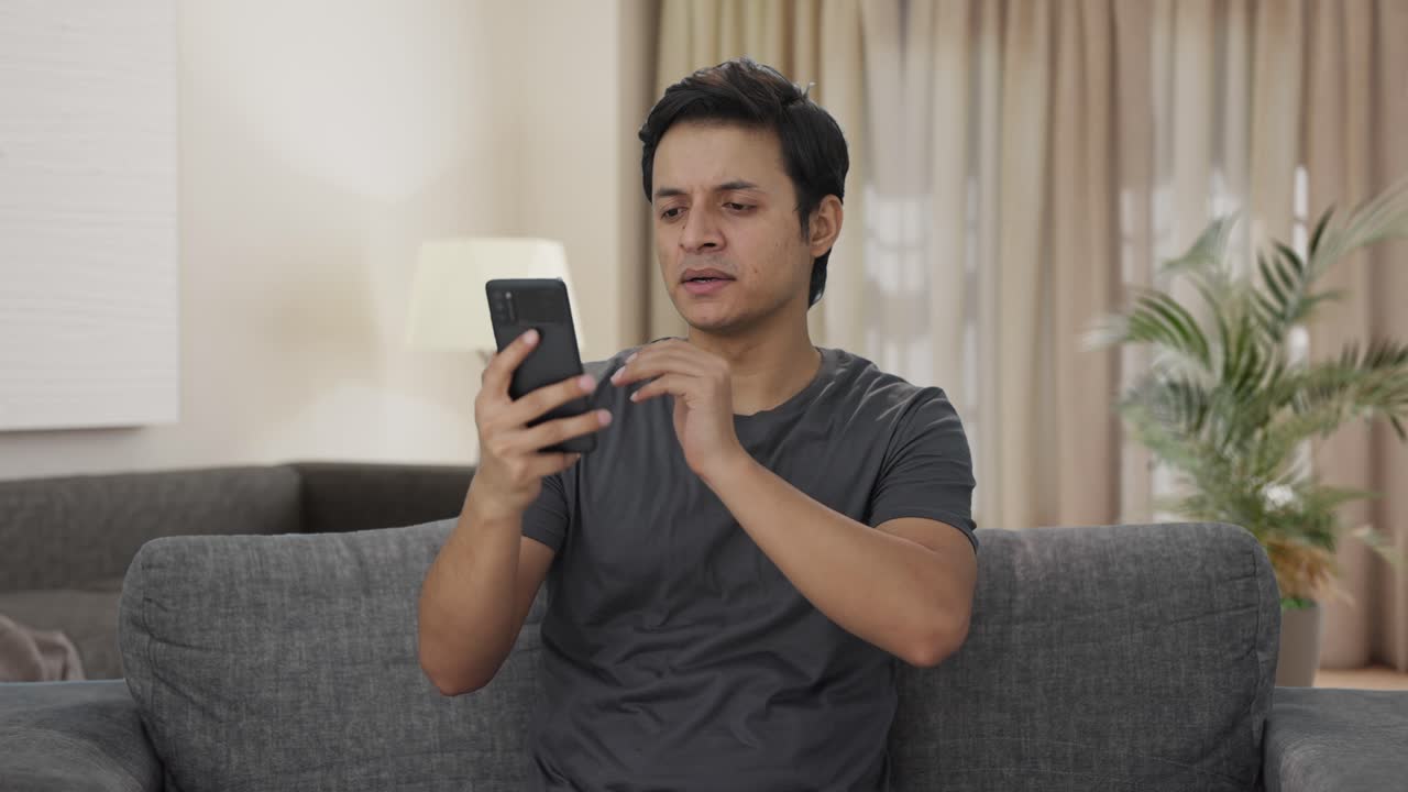 피곤한 인도인 남자가 전화를 스크롤하고 있습니다.