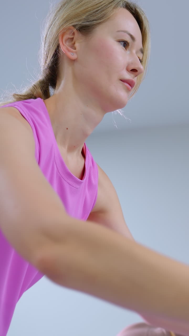 primer plano de una mano de mujer sosteniendo un rodillo de espuma, extendiéndose hacia adelante, con otra persona regresando a una posición normal y equipos de gimnasio en el fondo