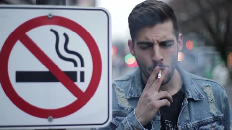 a contradiction in the urban landscape: a man smokes while standing next to a no smoking sign, highlighting the tension between regulations and personal choices