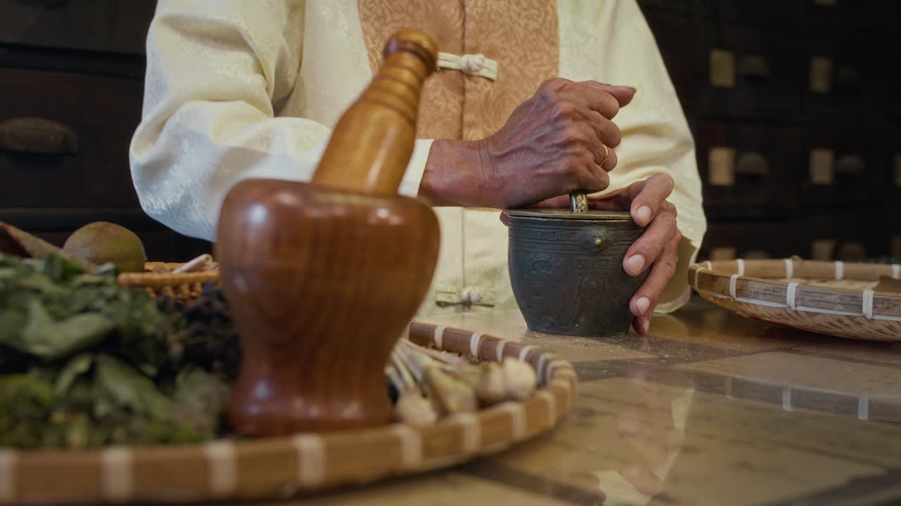 Senior Asian Traditional Medicine Practitioner Grinding Herbs in Mortar