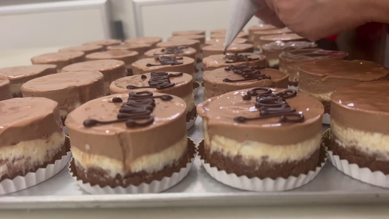 Close-up view of the hands of a skilled pastry chef writing names in his chocolate cakes inside his traditional workshop.4K 60FPS