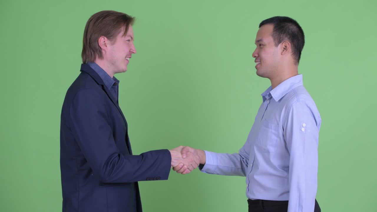 dos hombres de negocios teniendo un apretón de manos mientras sonríen contra el fondo verde del estudio
