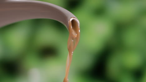 close up of freshly brewed brown coffee pouring from spout of a porcelain kettle against blurry background