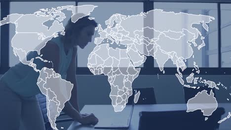 Animation-of-world-map-against-caucasian-woman-using-laptop-at-office