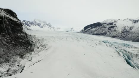 stunning aerial view of svinafellsjokull glacier framed by snow-capped peaks and a large muddy lagoon, highlighting iceland’s raw beauty.