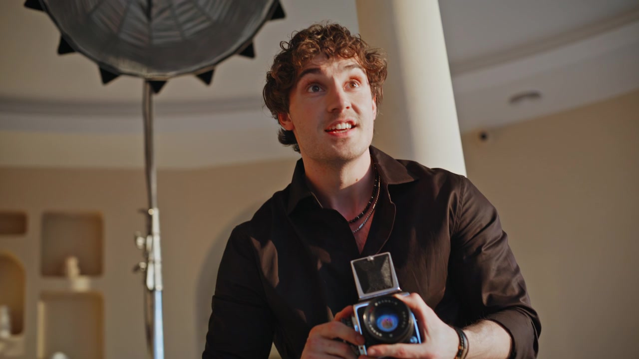 Cheerful photographer gesturing camera in studio. Man reviewing shots smiling.