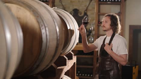 authentic shot of successful male sommelier is tasting a flavor and checking white wine quality poured in transparent glass in a wine cellar.