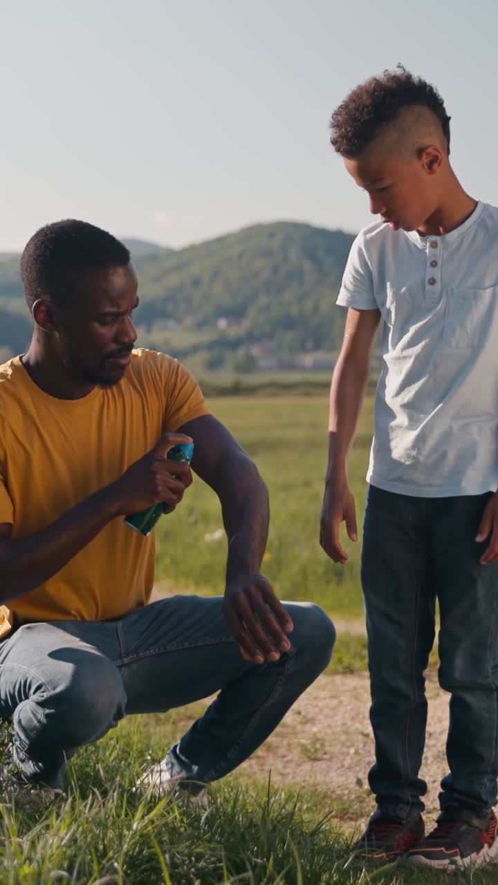 Afroamerikansk far påfører insektmiddel på sin søn i nærheden af et skilt med en advarsel om flåter under en