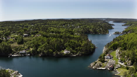 aerial drone shot the fjords and forests around lillesand, norway. fjords can be seen continuing into the distance as boats travel along them and houses long the shoreline.