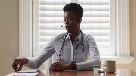 Portrait-of-african-american-female-doctor-wearing-phone-taking-notes-while-having-a-video-call