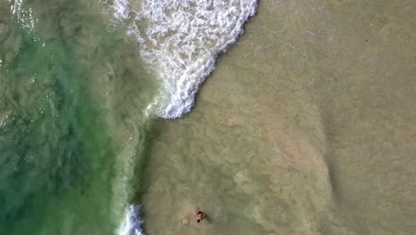 Milky,-frothy-seawater-churns-sediment-with-crystal-clear-seawater-in-stunning-drone-shot-from-above-of-waves-breaking